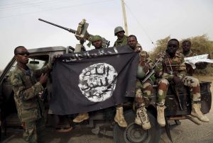 Nigerian soldiers hold up a Boko Haram flag that they had seized in the recently retaken town of Damasak, Nigeria, March 18, 2015. Chadian and Nigerien soldiers took the town from Boko Haram militants earlier this week. The Nigerian army said on Tuesday it had repelled Boko Haram from all but three local government districts in the northeast, claiming victory for its offensive against the Islamist insurgents less than two weeks before a presidential election. Picture taken March 18.    REUTERS/Emmanuel Braun - RTR4TZO2