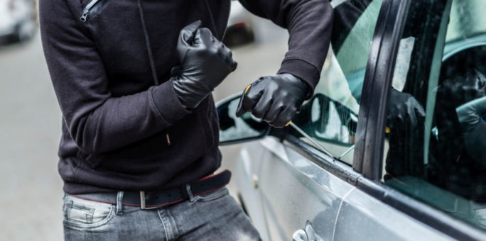 The man dressed in black with a balaclava on his head trying to break into the car. He uses a screwdriver. Car thief, car theft concept